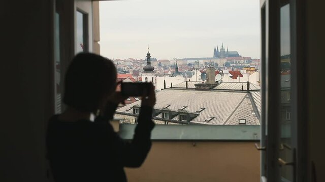 Silhouette oa woman takes photo of city on smartphone for transmission to subscribers using mobile Internet. Standing on balcony, she watches the panorama city through phone screen.