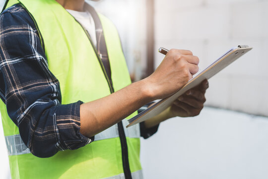 close up hands of inspector waer safety vest and checking list into clipboard