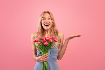 Excited blonde woman with tulips celebrating spring holiday, holding something on pink background,...