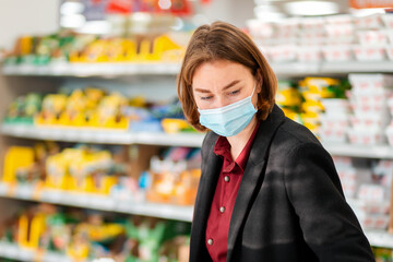 Shopping. Portrait of a young woman in a medical mask choosing products in a supermarket. The concept of shopping and the new normal