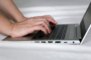 Female hands on laptop keyboard on a bed. Woman working at a ultrabook at home, remote work