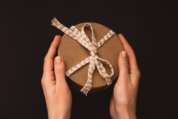 Colorful gift with beige rope in woman's hands on a dark background