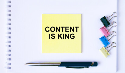 Yellow sticker with text Content is King lying on a white Notepad with a pen and paper clips