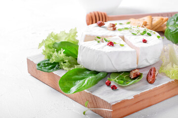 Brie cheese served with spinach, lettuce, pecan nuts, thyme and honey on the cutting board