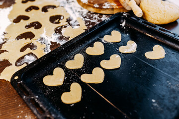 Obraz na płótnie Canvas Cookies in shape of heart for the Saint Valentine's Day. Dough, flour, baking pan and rolling pin on the table.