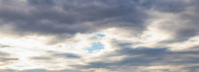 Fototapeta premium Through the dark clouds in the sky you can see a piece of blue sky, panorama