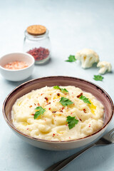 Mashed cauliflower with butter, pink peppercorns and parsley on concrete background