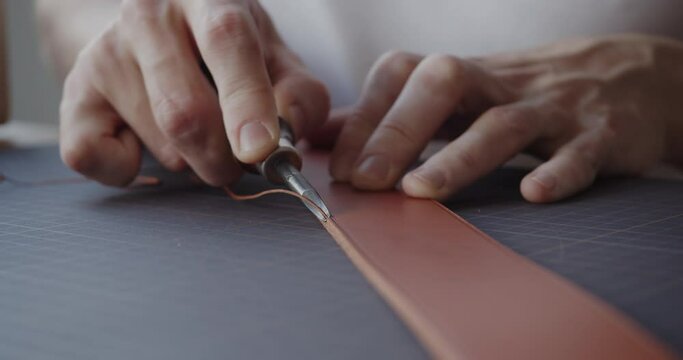 Making handmade leather belt. Young leather worker using leather edge beveler during belt manufacturing process in his workshop. Close-up shot.