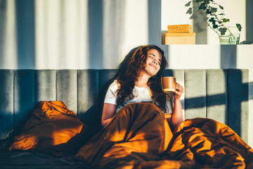 Woman drinking coffee in her bed at sunny morning.