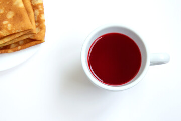 Red hibiscus tea in a white cup with delicious pancakes on a plate isolated on white background