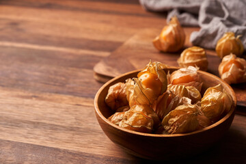 concept of cape gooseberry or physalis berry in a wooden bowl on a dining table in homemade style background with copy space                    