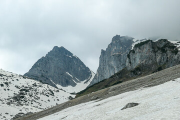 A panoramic view on the Alpine peaks in Austria from Marstein. The slopes are mostly covered with snow. Stony and sharp mountains. Overcast. Baren slopes, green valley below. Serenity and calmness