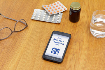 Schmerzmanagement-Konzept: Schmerztagebuch-App auf Handy oder Smartphone mit Wasserglas, Brille und...