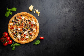 Tasty vegetable pizza and cooking ingredients tomatoes and basil on black background. Top view
