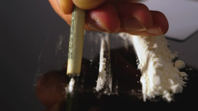A rolled banknote snorting a line of cocaine powder. Drug Abuse. Sniffing Cocaine lines. White powder on black table. Macro shot.