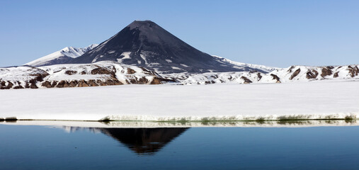 View of the Karymskaya Sopka and the reflection of the volcano cone in the lake water.