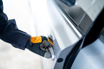 Male auto mechanic hand wearing protective glove holding car door handle in auto service garage. Mechanical maintenance engineer working in automotive industry. Automobile servicing and repair