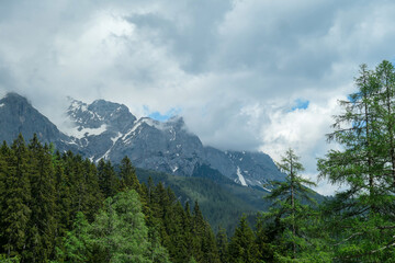 Obraz premium A panoramic view on the Alpine peaks in Austria from the Marstein. The slopes are still partially covered with snow. Stony and sharp mountains. Overcast. Baren slopes, dense forest at the foothill.