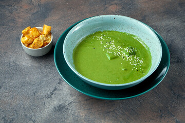 Healthy spinach cream soup with croutons in a blue bowl on a dark background