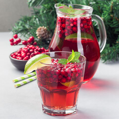 Punch or limeade with lingonberry and lime in a glass and pitcher on a gray background, square