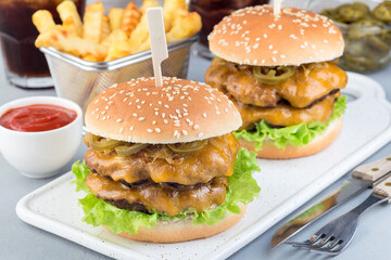 Double cheese burger with caramelized onion, lettuce and jalapeno, served with french fries and soda, on white plate, horizontal