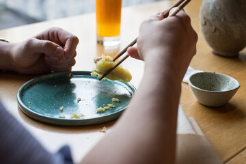 A person eating sushi at a restaurant. Visible hands holding chopsticks.