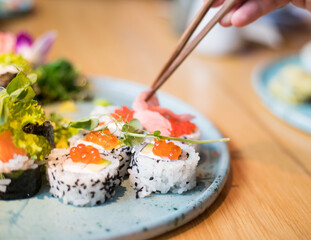 A person eating sushi at a restaurant. Visible chopsticks reaching for sushi.