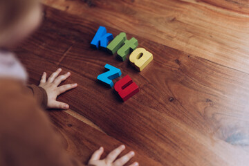 Kleinkind spielt mit Holzbuchstaben Schriftzug auf Holztisch - obrazy, fototapety, plakaty