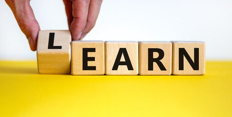 Learn or earn symbol. Businessman hand turns a cube and changes the word 'earn' to 'learn'. Beautiful yellow table, white background. Business and learn or earn concept. Copy space.