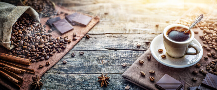 Coffee cup with coffee, coffee beans, cinnamon, star anise on an old wood desk in a coffee shop. Wide image in retro style.