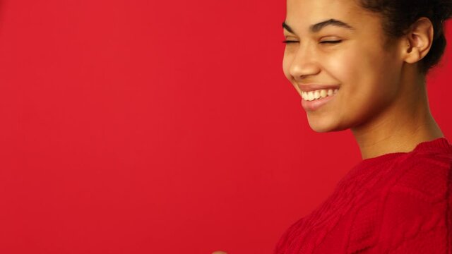 Mask off. Side view of beautiful mixed race girl taking off protective face mask, turning her head to the camera and smiling isolated over red background. Safety, coronavirus concept