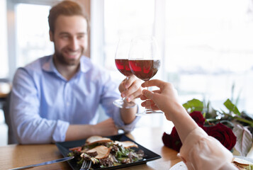 Romantic young couple with glasses of red wine toasting each other, celebrating Valentine's Day in restaurant