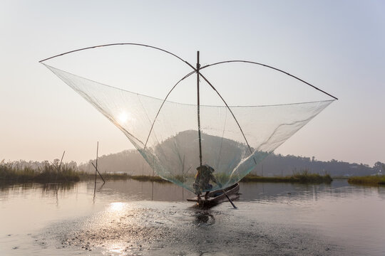 Fisherman on his boat moving arched swing nets above the water at  Loktak Lake