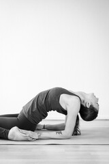 Black and white vertical view of a brunette young woman practicing yoga indoors in her home interior, doing a backbend asana variation.