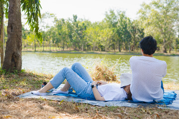 asian couple picnic and relax with happiness feeling in park with lake in springtime