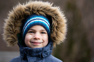 Portrait of smiling preschool boy in coat with fur hood in winter