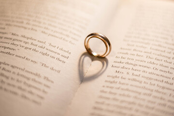 Fototapeta premium Two wedding rings on the book cast shadows in the form of hearts. Valentine's Day. Romance.
