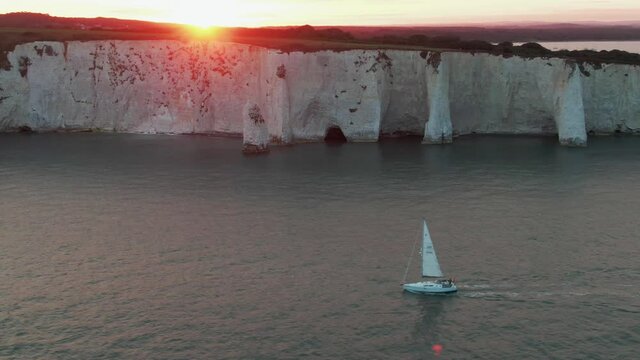a lonely sailing boat in front of beautiful limestone cliffs near old harry rocks in south england, united kingdom while sunset