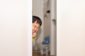 Fototapeta na wymiar A playful boy peeking from behind the door.