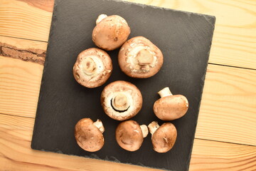 Several organic fresh, cream mushrooms with a slate board, close-up, on a wooden table.