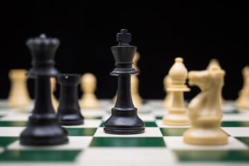 Extreme close up of chess pieces arranged on a portable chessboard before a black background.
