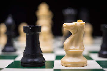 Extreme close up of chess pieces arranged on a portable chessboard before a black background.