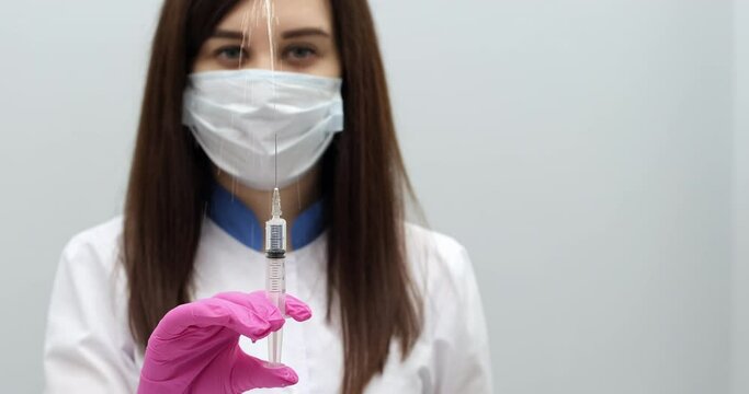 A nurse wearing a mask and pink gloves, who makes a fountain of medicine from a needle in front of her, pressing a syringe. Half of the frame is allocated for text and graphics.