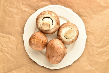 Several organic fresh, cream mushrooms on a ceramic plate, close-up, on wrapping paper.