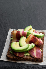 Sandwich with plant-based bacon rashers and avocado on black stone background