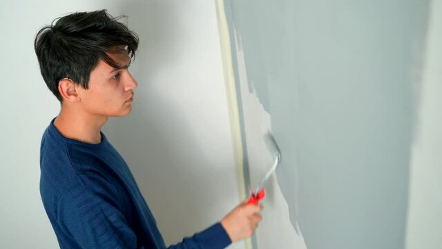 A hearing-impaired young man in hearing aids paints the wall with a roller gray.