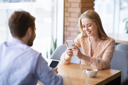 Joyful Millennial Couple Using Smartphones On Date At Coffee Shop, Checking Messages Or Chatting Online