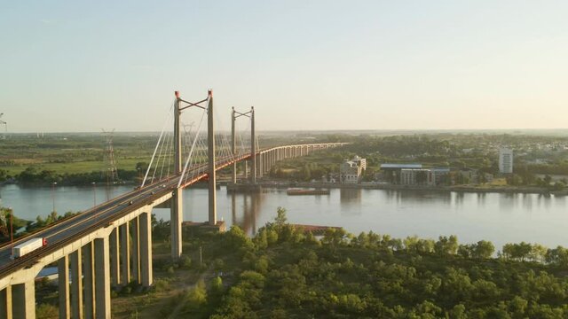 Aerial shot flying alongside cable-stayed bridge crossing a big river at golden hour
