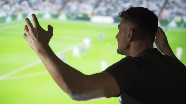 A man cheerleader is watching a sports match on the background of the screen. The soccer fan cheers for his team in the interior. Viewing sports events