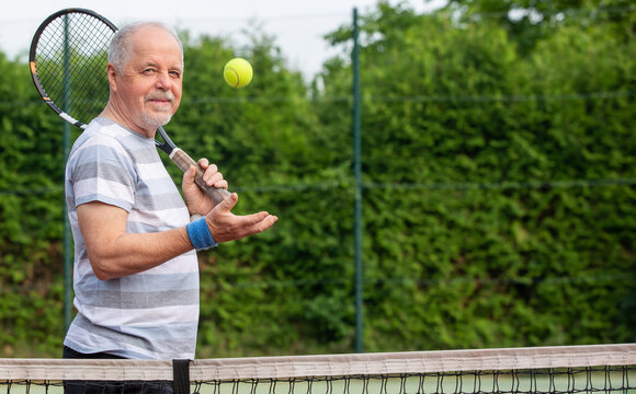 Portrait of an active senior man at the tennis court with racket and tennis ball, sport concept